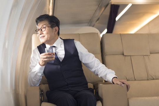 Senior businessman drinking whiskey on airplane