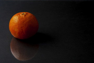 Mandarin orange isolated on dark black background with reflection. Space for text.Citrus reticulata, also known as the mandarin or mandarine, is a small citrus tree with fruit resembling other oranges