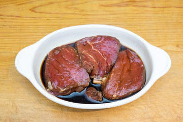 Beef steak eye fillet meat marinading in white dish of soy sauce on wooden background with copy space