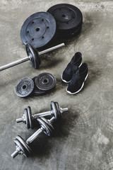 Obraz na płótnie Canvas dumbbells and barbell with weight plates and sneakers on grungy grey floor