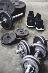 Obraz na płótnie Canvas dumbbells and barbell with weight plates and sneakers on concrete floor