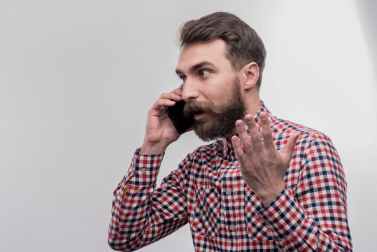 Phone conversation. Image without face retouching with bearded dark-haired man feeling angry while having phone conversation