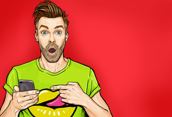 Attractive amazed young man pointing finger on mobile phone in comic style. Pop art surprised guy holding smartphone.  - obrazy, fototapety, plakaty