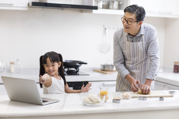 Happy little girl and grandfather baking cookies in kitchen