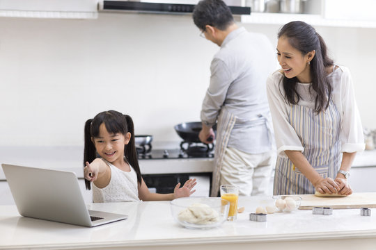 Happy little girl and grandparents baking cookies in kitchen