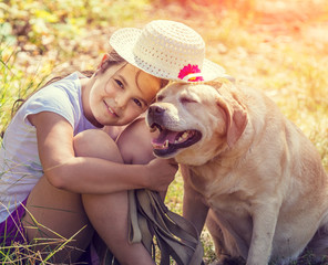 Portrait of the happy young girl hugging dog outdoors in the forest in summer. Dog and girl wearing one sun hat together