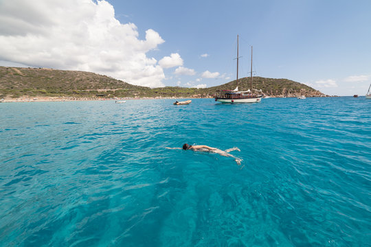 Seascape with swimming woman and some boats turquoise sea of Mari Pintau - Sardinia - Italy