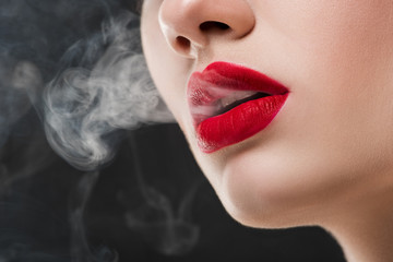 cropped view of girl with red lips blowing smoke, isolated on grey © LIGHTFIELD STUDIOS