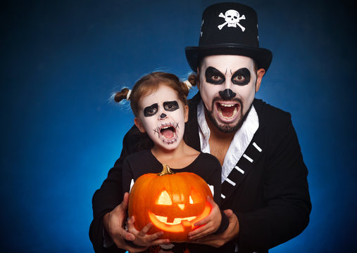 family father and daughter in costumes and make-up to Halloween with pumpkin.