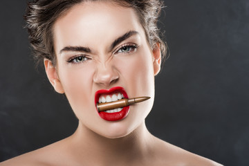 aggressive elegant woman holding bullet in teeth, isolated on grey