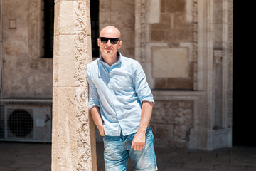 Bald man in sunglasses walking on old narrow street