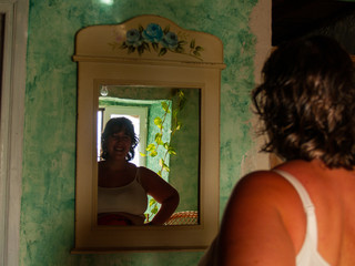Reflection in the mirror of a young woman smiling in a rural house with green wall