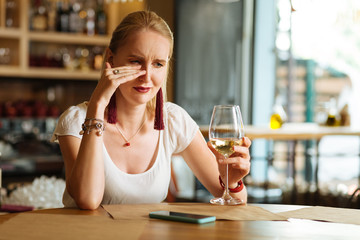 I am all alone. Sad cheerless woman drinking wine while crying in the restaurant