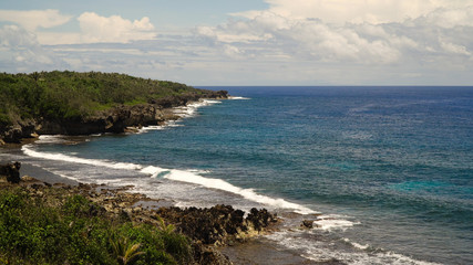 Rocky beach with palm trees, blue water on a tropical island. Sea rocky coast, waves breaking to the rocky shore. Viewpoint along stony beach with rocks.Stony sea beach scene. Philippines. Travel