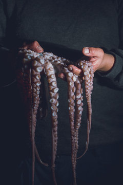 Man holds a raw octopus in his hands. Dark photo
