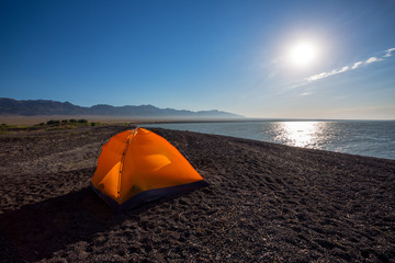 Orange tourist tent in the lake shore under the dramatic sunset sky