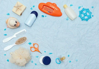 Bath products flat lay. top view of children's bathing things: shampoo, water thermometer, comb, washcloth, cream, rubber duck, dummy, soap, oil, scissors with space for text on a blue background