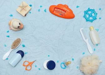 Bath products flat lay. top view of children's bathing things: shampoo, water thermometer, comb, washcloth, cream, rubber duck, dummy, soap, scissors with space for text as a frame