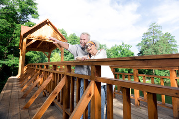 Having rest. Couple of retired man and woman feeling extremely relieved while having rest standing on big wooden bridge