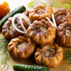 Fried meat pies belyash with vegetables on wooden board