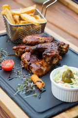 Delicious BBQ chicken wings served with Coleslaw salad and french fries on cutting board