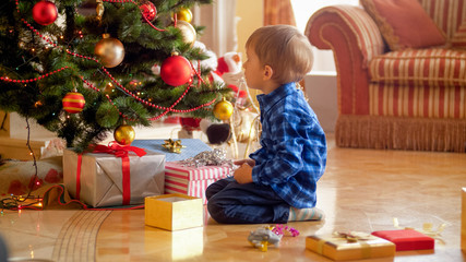 Little toddler boy looking on christmas tree at morning