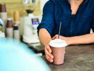 Hand gives cup to client visitor. Enjoy your drink. Man receive drink at bar counter. Cappuccino or cacao with straw. Served in paper cup coffee to go. Hand of barista at bar serve coffee for client