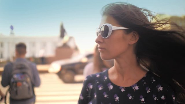 Young Beautiful Brunette Woman In Sunglasses Looking At Camera, Crowd Of People On Summer City Street In Background. Closeup, Shallow DOF, Slow Motion, 4K UHD.