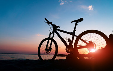 Fototapeta na wymiar Beautiful close up scene of bicycle at sunset, sun on blue sky with vintage colors, silhouette of bike forward to sun