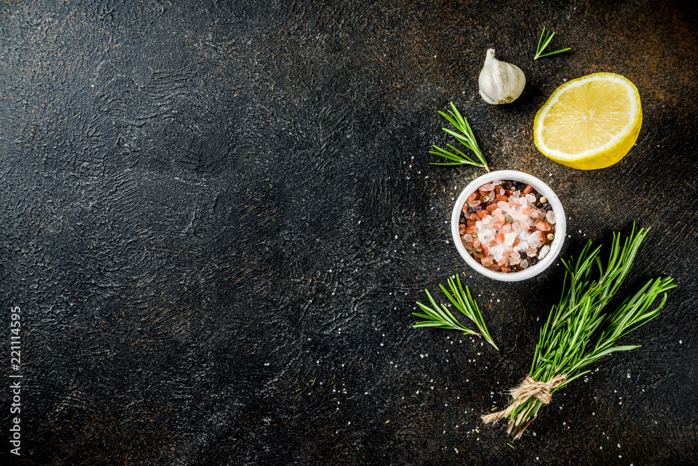 Wall mural Cooking food ingredients background. Spices, garlic, herbs, olive oil. rusty black stone table. Copy space above