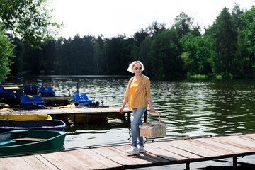 Woman in glasses. Elderly woman wearing glasses holding hamper for picnic in hand while crossing the bridge