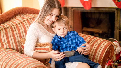 Smiling young mother with her son watching cartoons sitting in armchair at living room