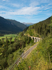 Train and the bridge in Switzerland with green slopes. The Rhaetian Railway section from the Albula/Bernina area (the part from Thusis to Tirano, including St Moritz), August, 2018