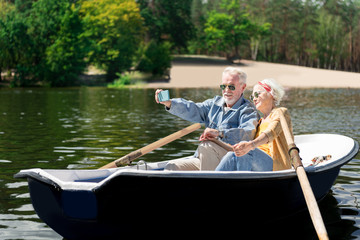 Fototapeta na wymiar Making selfie. Modern elderly man holding his blue smart phone while making selfie with his beautiful smiling wife