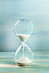 A side view of an hourglass with falling sand, on a teal background with copy space