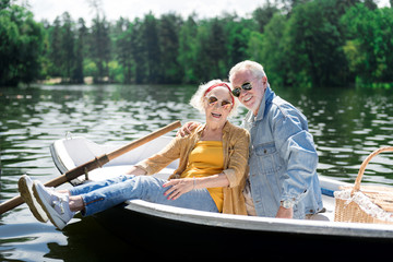 Smiling pensioners. Smiling cheerful pensioners feeling very happy while sitting in little boat while having romantic date