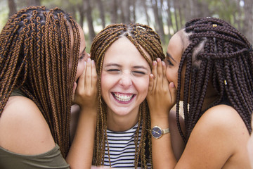 Three young and beautiful girls, with braided hair, laughing and whispering secrets
