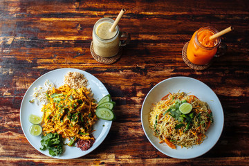 Healthy Vegetarian vegan menu Pad Thai, stir-fried rice noodles and singapore noodles and banana and carrot smoothies on wooden table.top view
