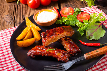 bbq spareribs on the plate with green salad and white sauce.