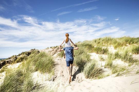 Netherlands, Zandvoort, father carrying daughter on shoulders in beach dunes