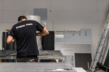 Young worker, operating a CNC machine. Big vinyl rolls ready for high quality printing. Industrial plotting service facility, International delivery system. Advertising and press business.