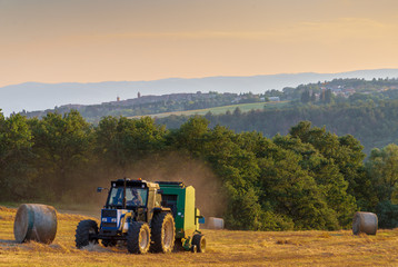 Obraz premium A hay baler at work in an Umbrian field as the sun sets.