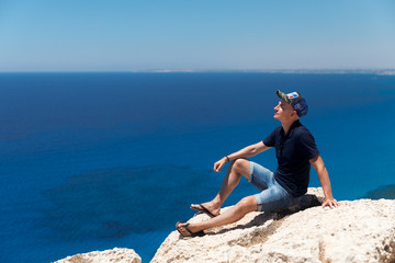 Bald man in a T-shirt and shorts sitting alone on top of a mountain overlooking the sea
