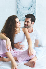 happy young couple in pajamas embracing on bed