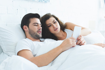 young couple lying in bed and using smartphone together