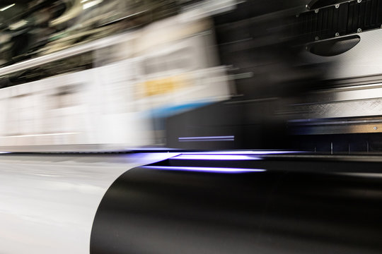 Massive print head flashing by while processing a big oversized roll of glossy premium paper in a professional plot and print facility.