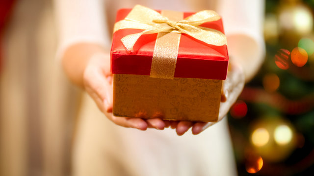 Closeup image of young woman in dress showing red present box in camera. Concept of Christmas gifts