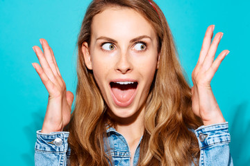 Close-up portrait of surprised excited cheerful girl on a blue background. The concept of surprise...