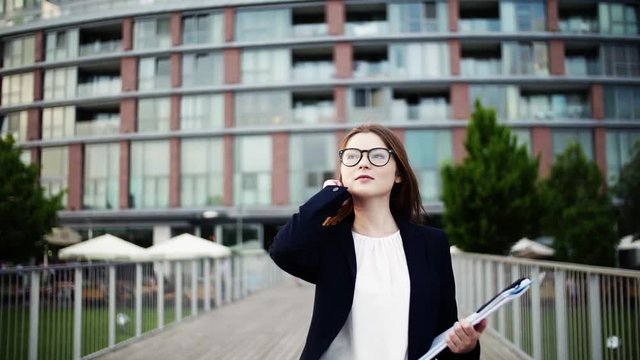 A young businesswoman with glasses walking on the bridge in a city.