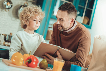 Delicious dish. Serious father and son checking a recipe while cooking